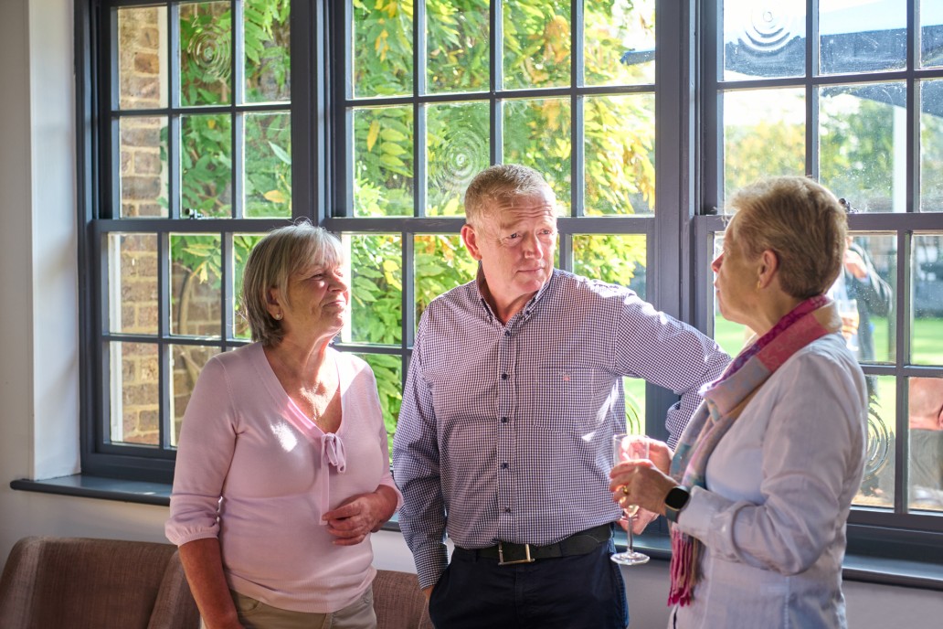Three Addington Palace Golf Club members standing and talking near a window in the clubhouse
