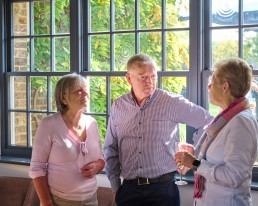 Three Addington Palace Golf Club members standing and talking near a window in the clubhouse